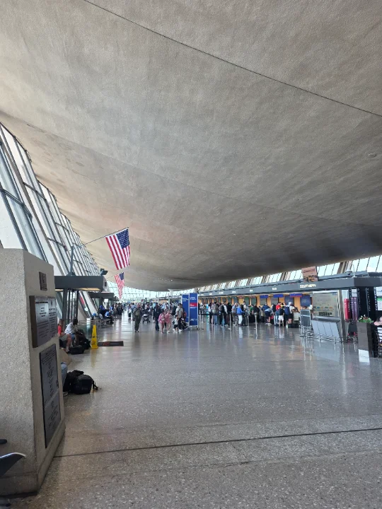 An airport terminal with a large American flag hanging from the ceiling.