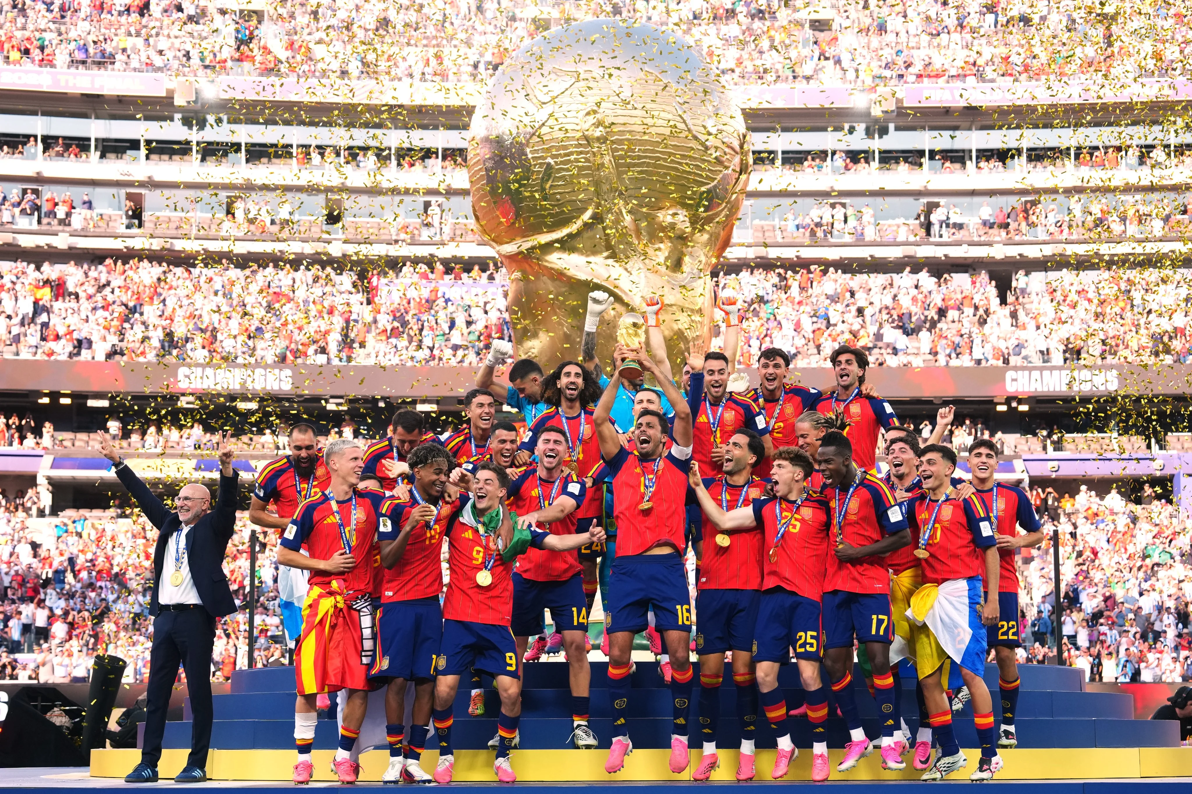 The Spanish national football team celebrates on a podium, lifting the UEFA European Championship trophy amidst a stadium crowd.