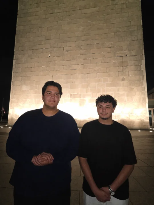 Two men standing in front of a tall stone monument at night.